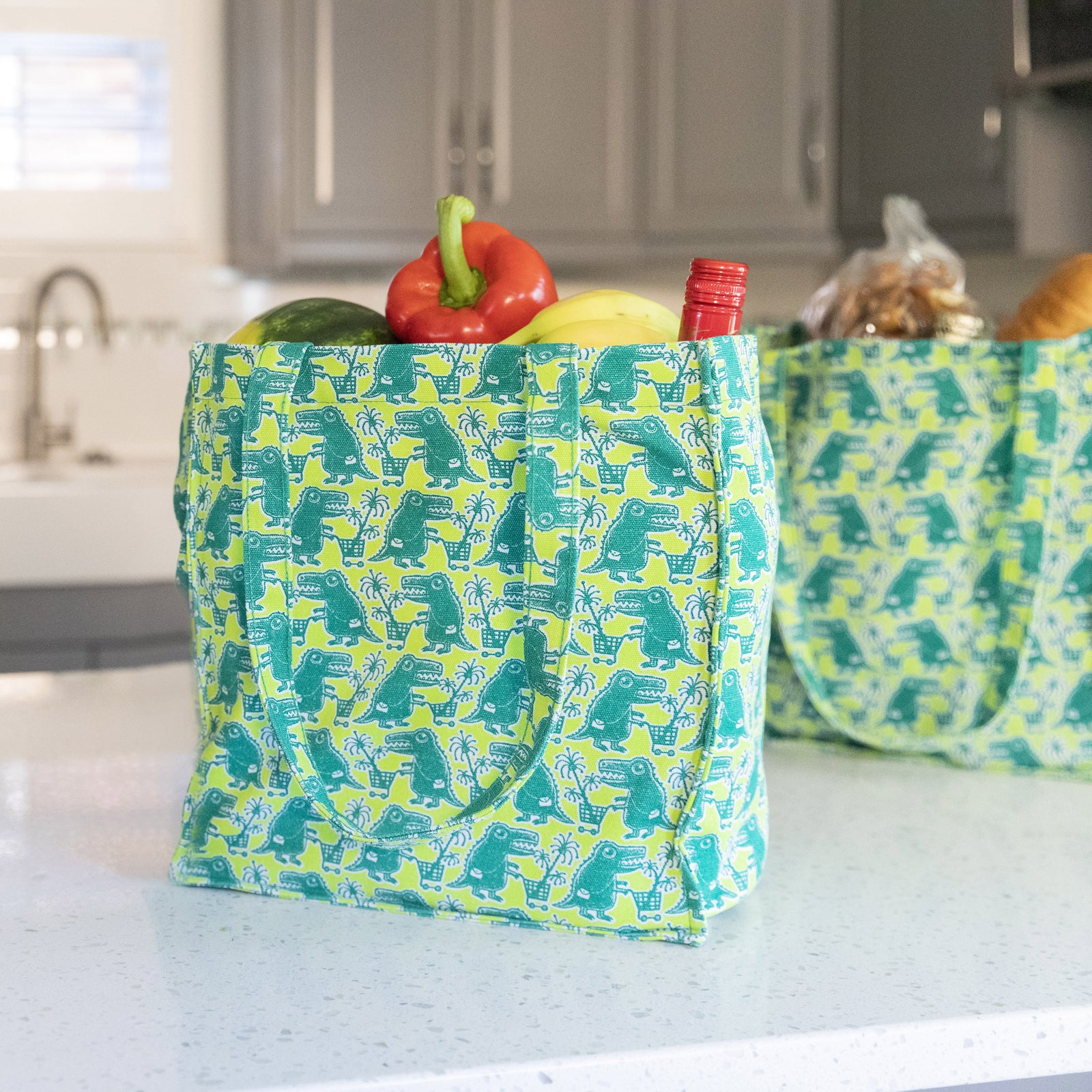 Gifts for the dinosaur lovers in your life, image of green and chartreuse shopping bag with dinosaur pushing shopping cart pattern.